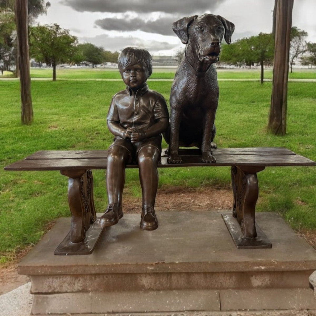  young boy and his loyal pet dog sitting side by side in the middle of a bronze bench. 