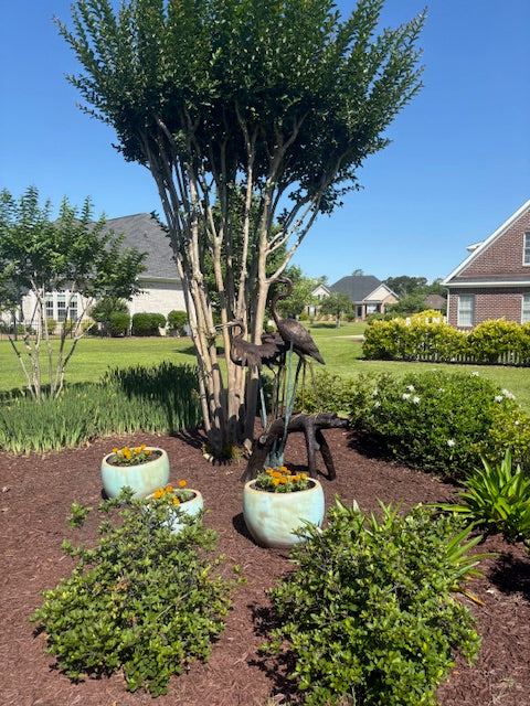 Bronze Statue of a pair of herons in garden view with flowers near house
