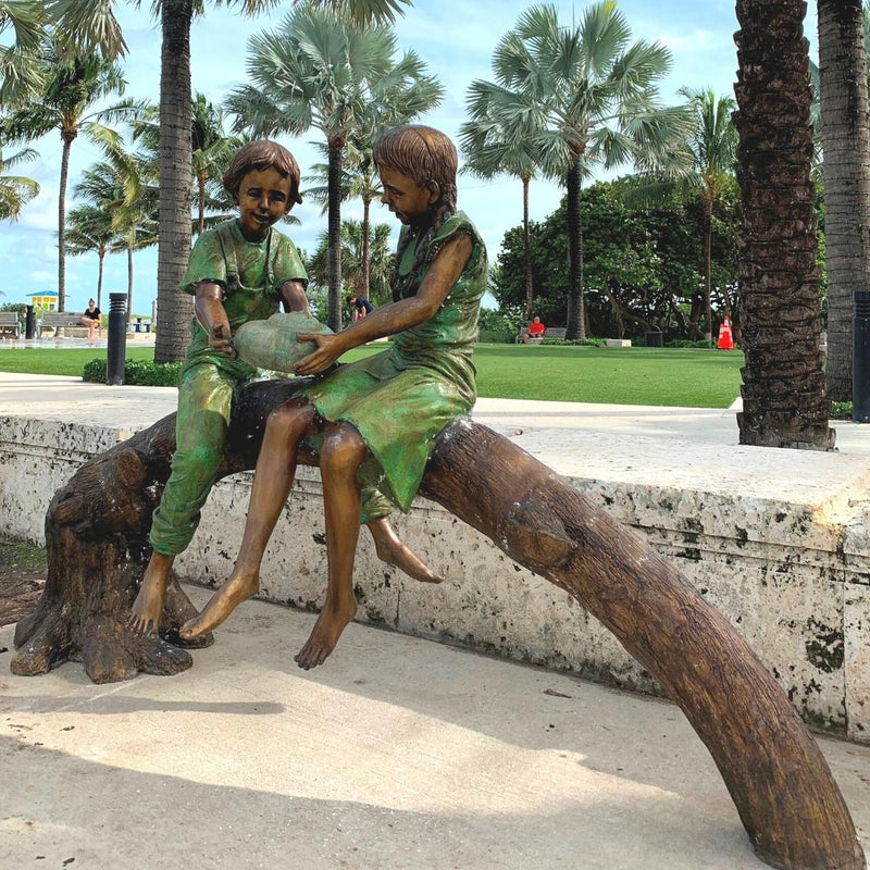 Bronze statue of two children sitting on a log holding a turtle